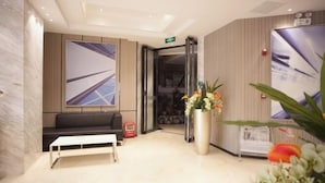 A modern lobby with a marble reception desk, a black sofa, a large abstract painting, a tall vase with flowers, and a glass elevator. - Queen Design Hotel (Qiandeng Lake Resort Guicheng Subway Station Branch) (Foshan)