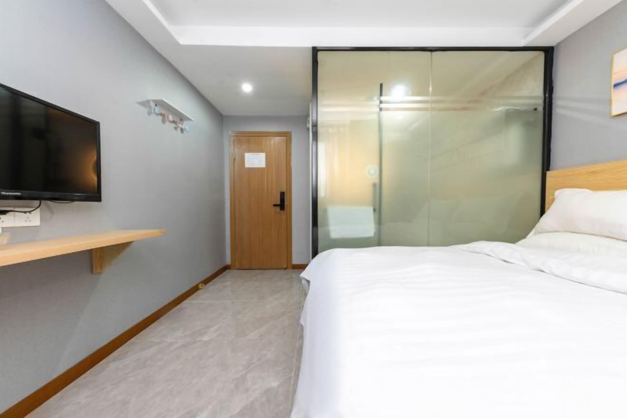 A hotel room with a bed, a TV mounted on the wall, a wooden door, and a glass partition.