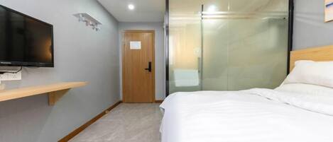 A hotel room with a bed, a TV mounted on the wall, a wooden door, and a glass partition.