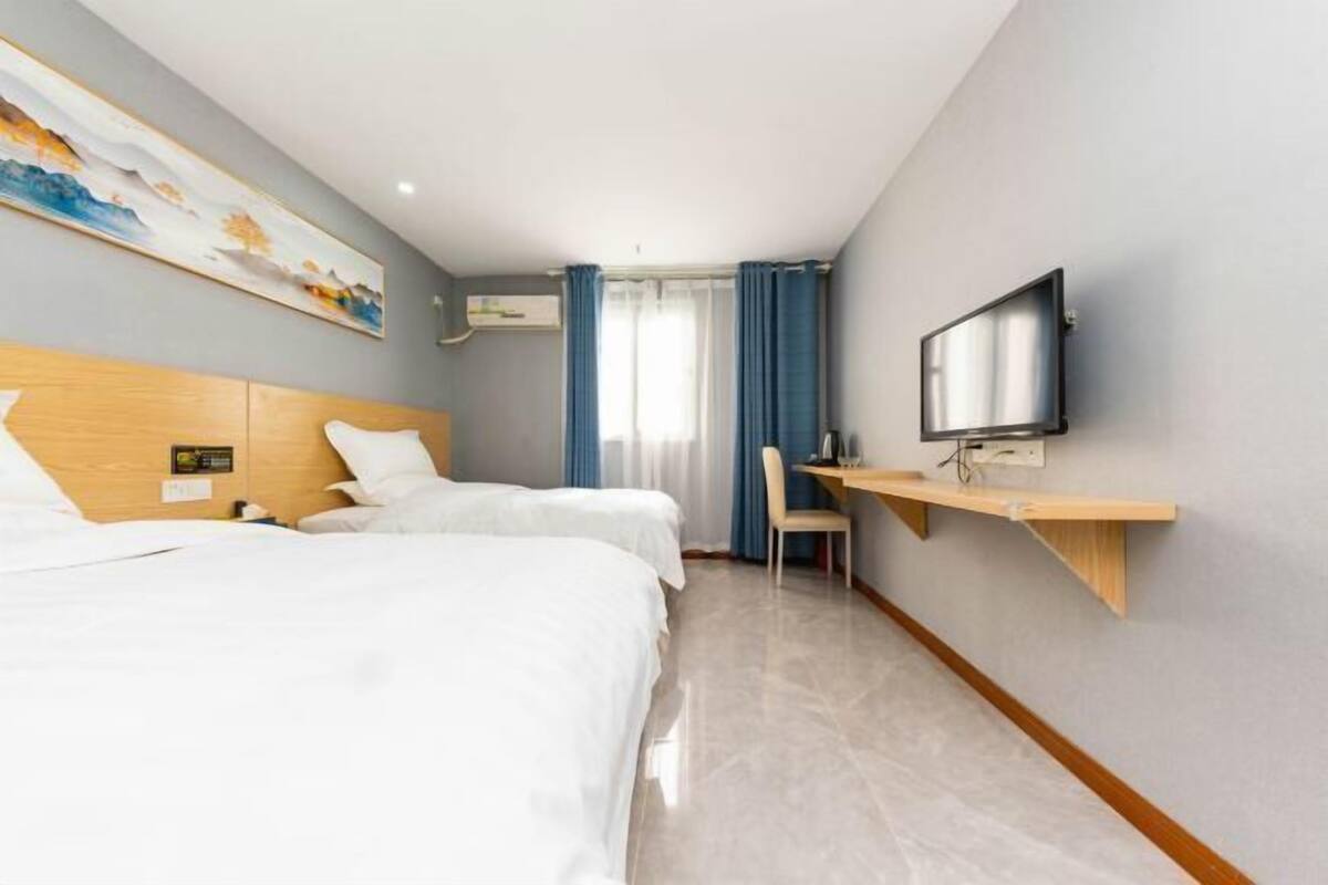 Een hotelkamer met twee bedden, een bureau, een televisie en een schilderij aan de muur.