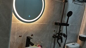 Een badkamer met een ronde spiegel, een wastafel, een handdouche en een toilet.