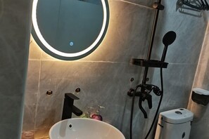 A bathroom with a round mirror, a sink, a handheld showerhead, and a toilet. - Dongsheng Boutique Hotel (Shenzhen)