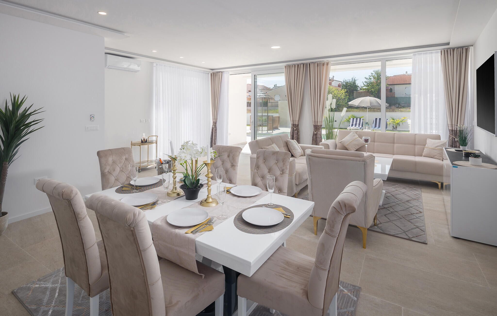 A modern dining area with a white table set for four, surrounded by beige upholstered chairs.