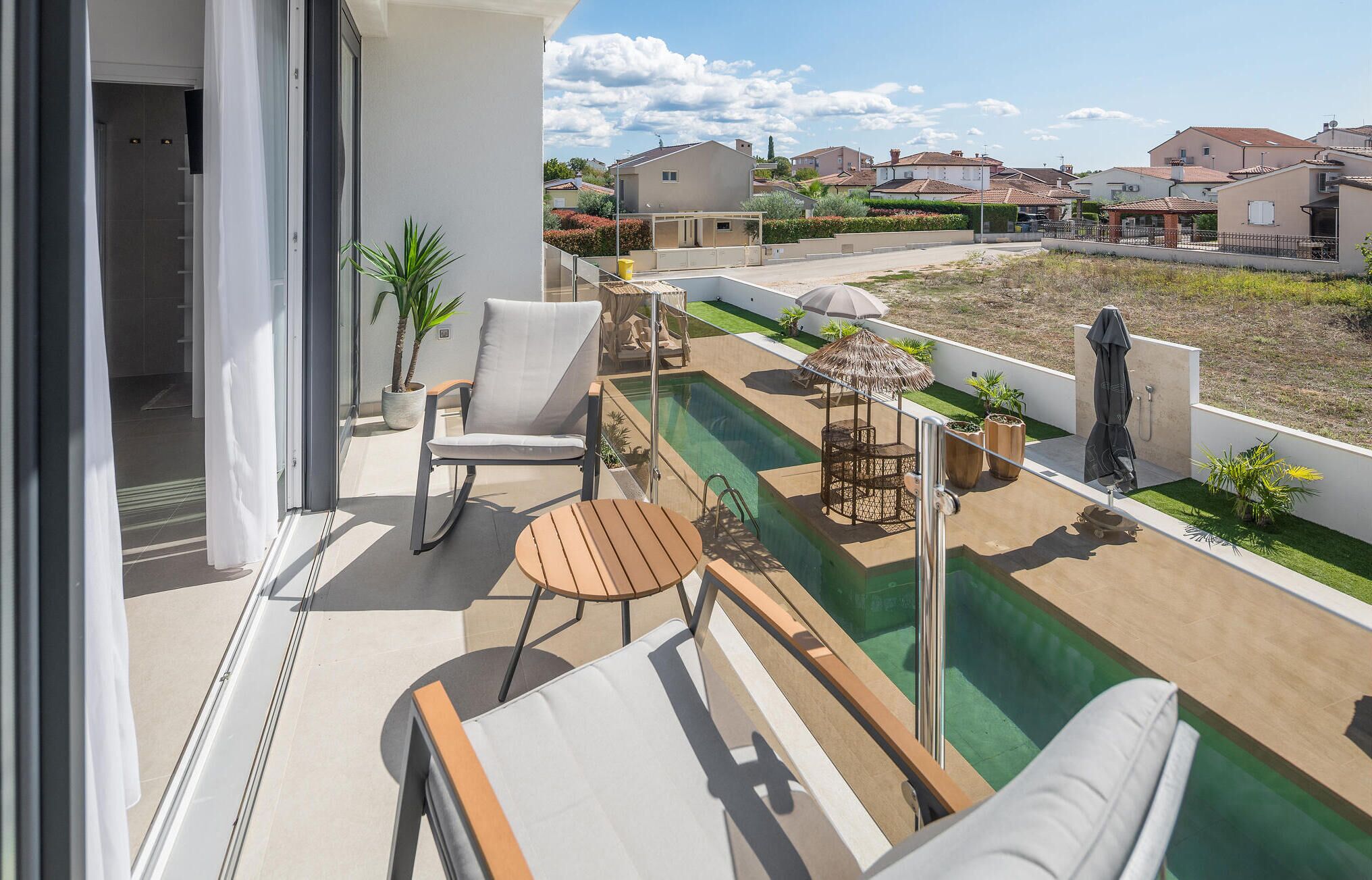 A balcony with a pool, lounge chairs, and a view of surrounding houses.