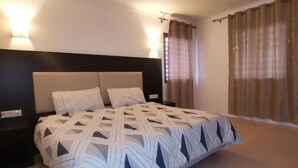 A bedroom with a bed, two bedside tables, a headboard, and a window with curtains. - Family spacious apartment with sea view, AC, WiFi, 7 mins walking to the beach (M'diq)