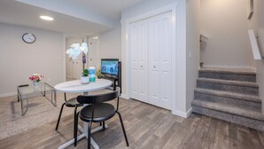 A modern living room with a round glass table, two black chairs, a white door, and a staircase. - 1 KING Modern Two Bedroom Secondary Suite in Airdrie Alberta (Airdrie)