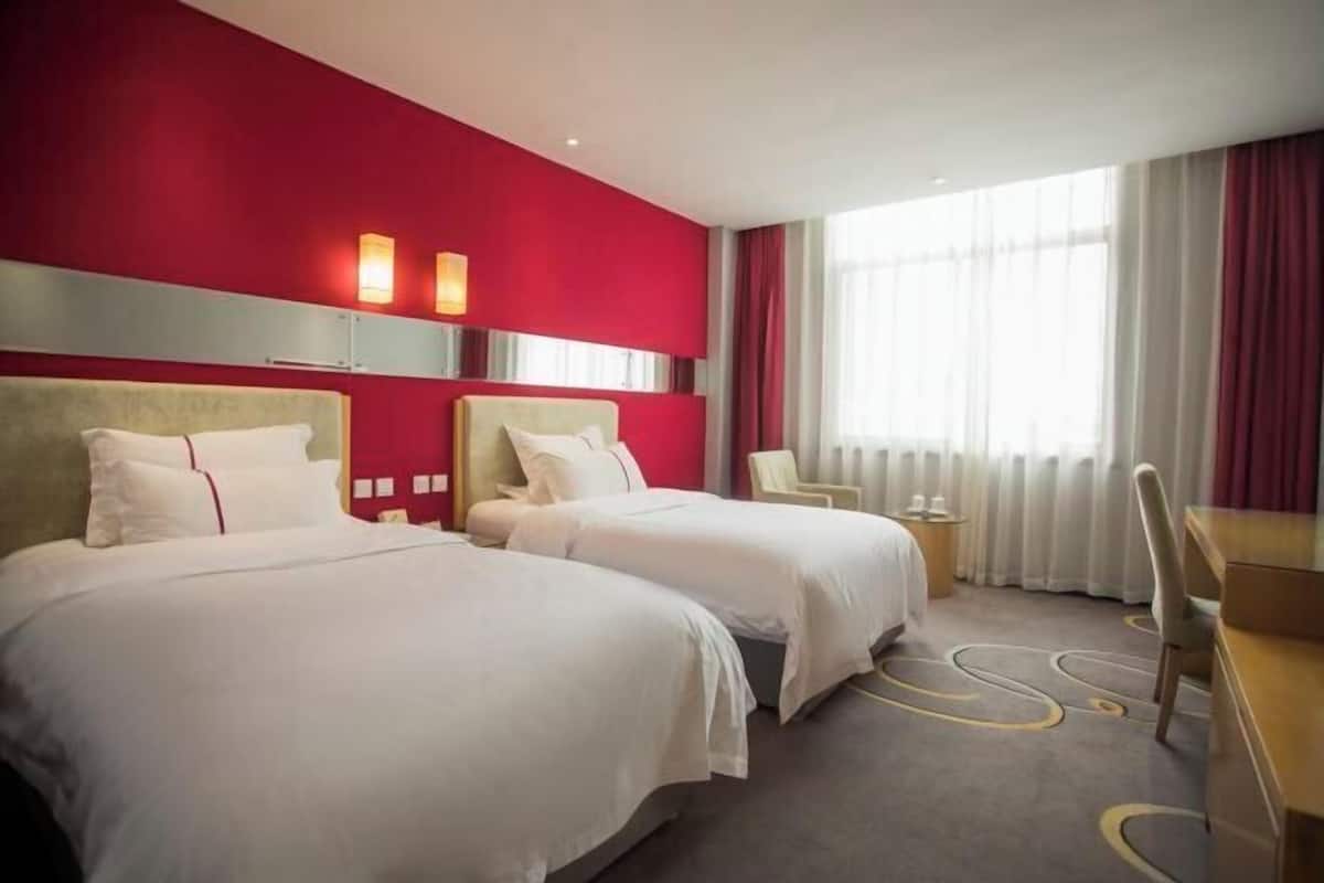 Een hotelkamer met twee bedden, een bureau, een stoel en een groot raam met gordijnen.