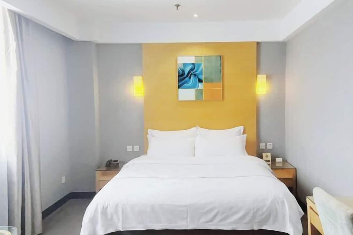 Een hotelkamer met een bed, nachtkastjes, een kunstwerk aan de muur en twee wandlampen.