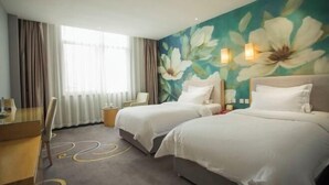 Ett hotellrum med två sängar, ett skrivbord, en stol och en stor väggmålning med blommotiv.