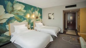 Ett hotellrum med två sängar, en väggmålning med blommotiv, en dörr och ett litet konstverk på väggen.