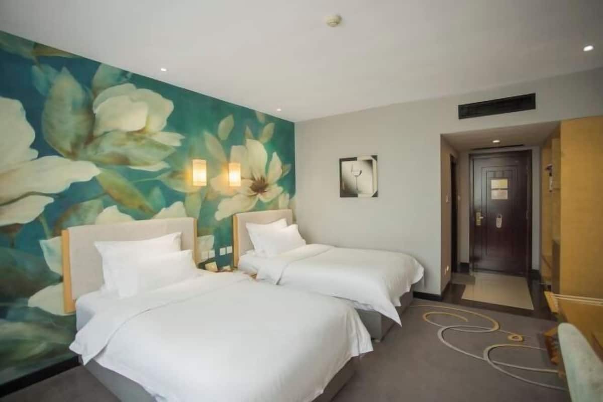 Een hotelkamer met twee bedden, een bloemmotief muurschildering, een deur en een klein kunstwerk aan de muur.