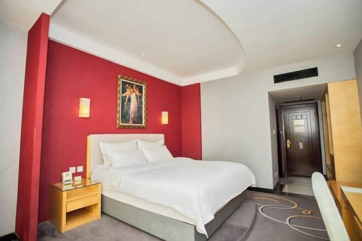Een hotelkamer met een bed, een nachtkastje, een rode accentmuur en een schilderij.