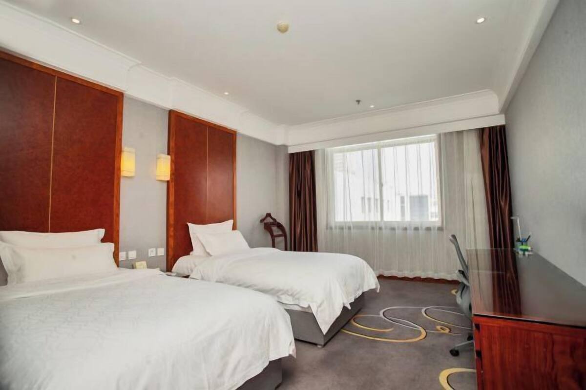 Een hotelkamer met twee bedden, een bureau, een stoel, een televisie en een groot raam met gordijnen.