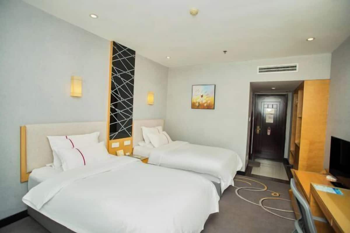 Een hotelkamer met twee bedden, een televisie, een bureau en een deur die naar een andere kamer leidt.