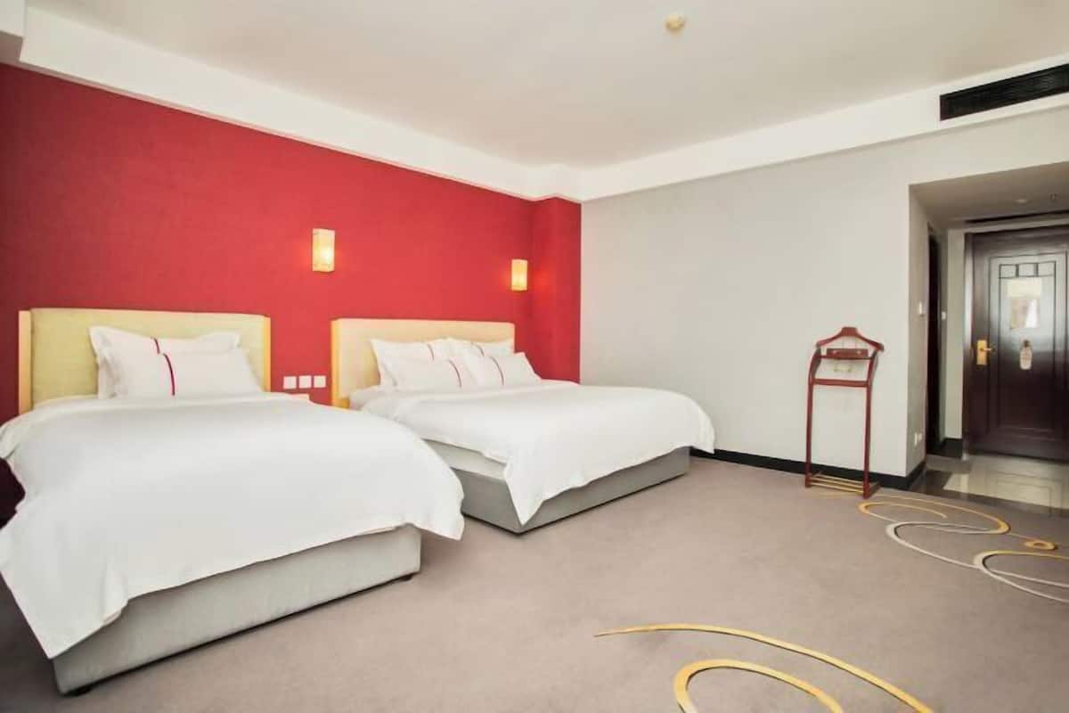 Een hotelkamer met twee bedden, een rode accentmuur en een deur aan de rechterkant.