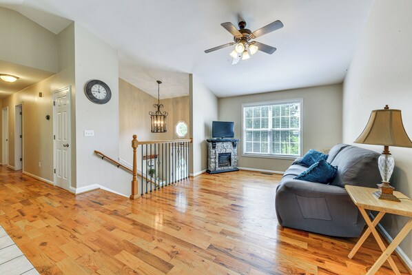 A spacious living room with hardwood flooring, a grey sofa, a fireplace, and a ceiling fan.