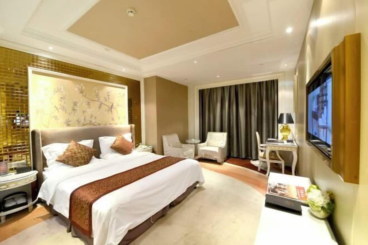 Ein Hotelzimmer mit einem großen Bett, einem Fernseher, einem Schreibtisch und einem Sessel.