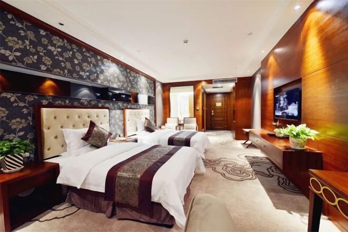 Ein Hotelzimmer mit zwei Betten, einem Fernseher, einem Schreibtisch und einem großen Fenster.