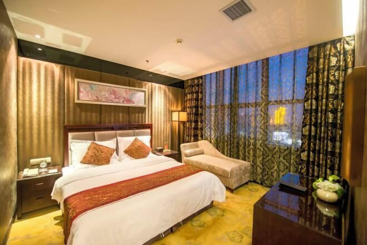 Ein Hotelzimmer mit einem großen Bett, einem Sessel, einem Schreibtisch und Blick auf den sternenklaren Nachthimmel durch Vorhänge.