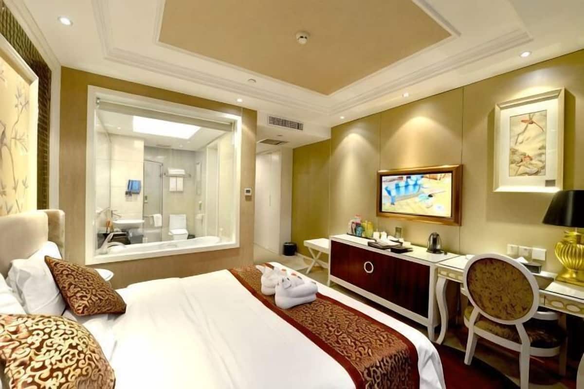 Ein Hotelzimmer mit einem großen Bett, einem Schreibtisch, einem Sessel, einem Fernseher und einem durchgegangenes Badezimmereingang.
