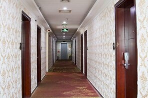 Un pasillo de hotel con papel tapiz estampado, puertas de madera y alfombra roja.