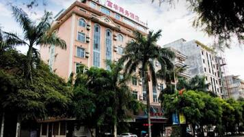 A hotel with a prominent sign, multiple floors, and a surrounding area with trees and parked cars.
