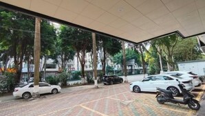 A covered parking area with cars and a scooter, surrounded by trees and buildings.