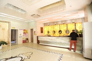Um saguão de hotel com balcão de recepção, um candelabro, um piso estampado e uma parede com quadros emoldurados.