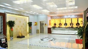 A hotel lobby with a reception desk, chandeliers, and a patterned floor.