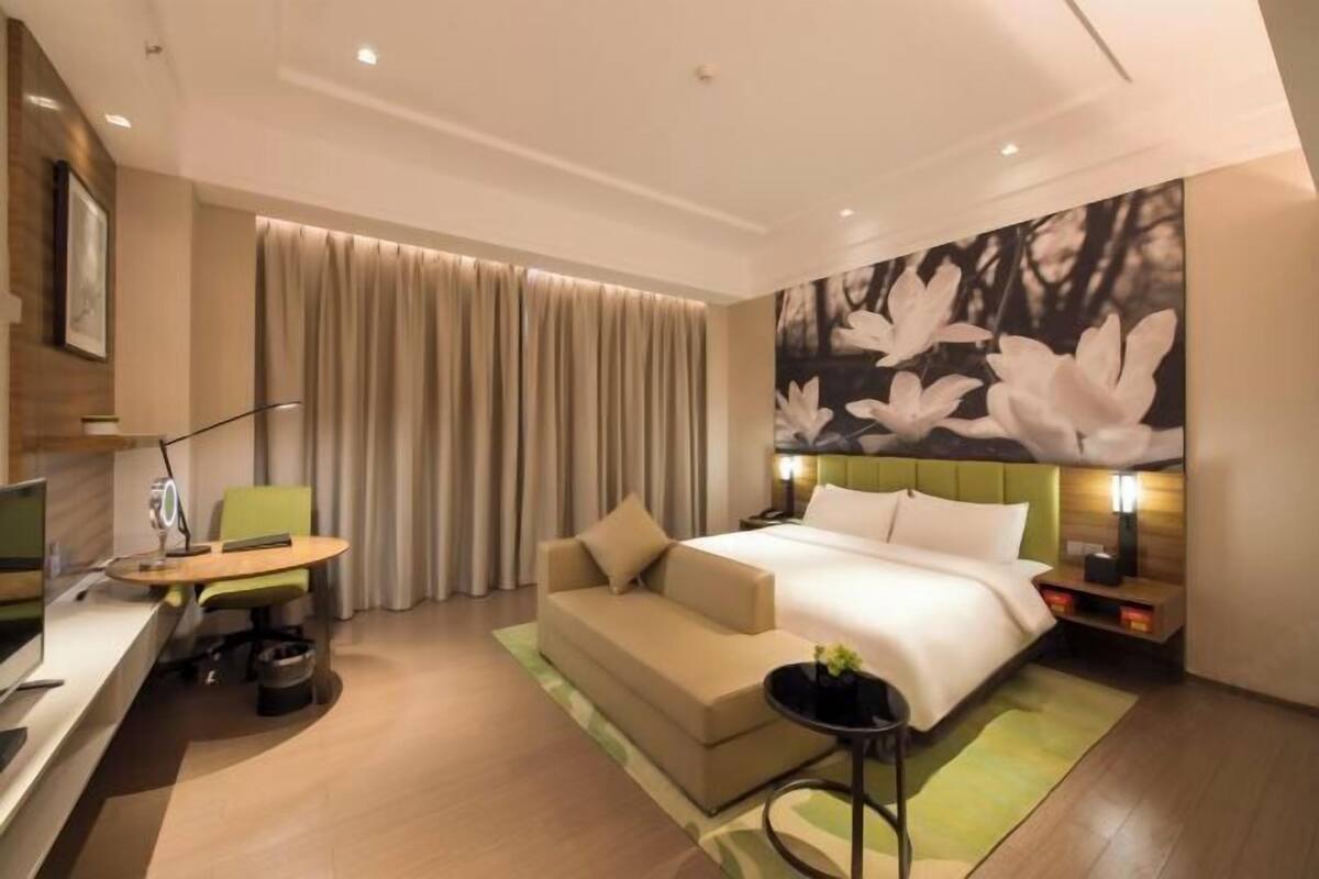 A modern hotel room with a bed, a desk, a sofa, and a large floral wall art piece.