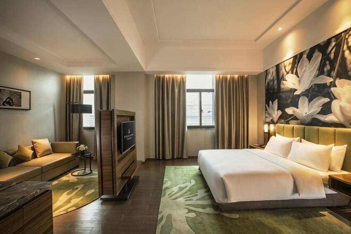 A hotel room with a bed, a TV, a sofa, and a large floral artwork on the wall.