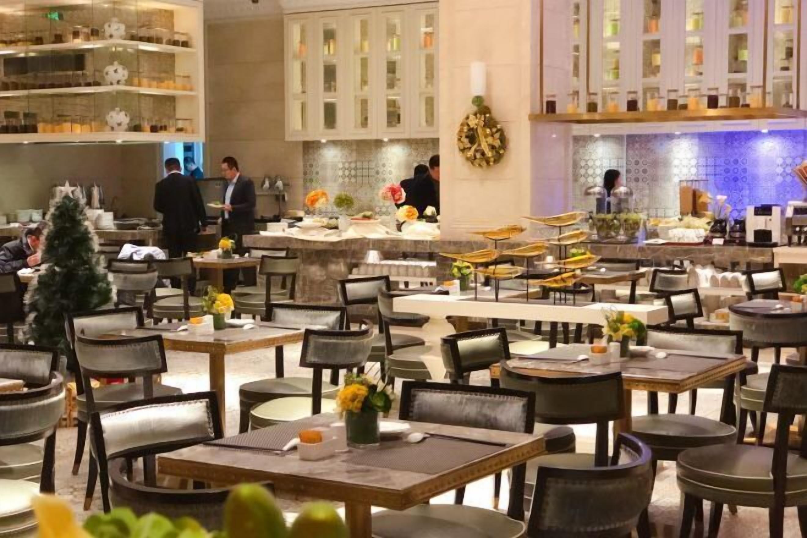 Een restaurant met meerdere eettafels en stoelen, een kerstboom en een keuken met personeel.