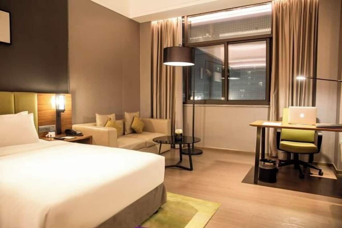 A hotel room with a large bed, a desk with a chair, a small round table, and a sofa.