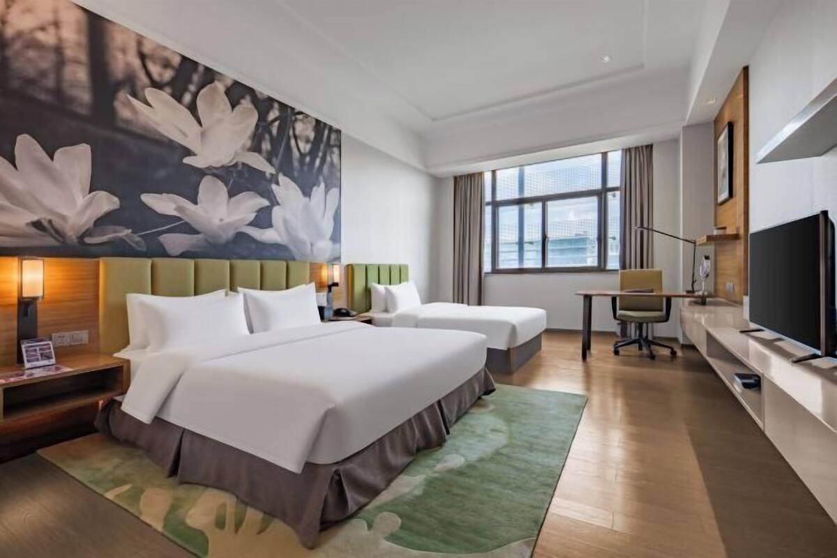 A hotel room with two beds, a desk, a chair, a TV, and a large window.