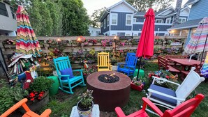 Un patio con sillas Adirondack de colores, un brasero y diversas plantas en macetas.
