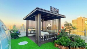 Un jardín en la azotea con zona de estar, césped artificial, plantas en macetas y vistas del horizonte de la ciudad.