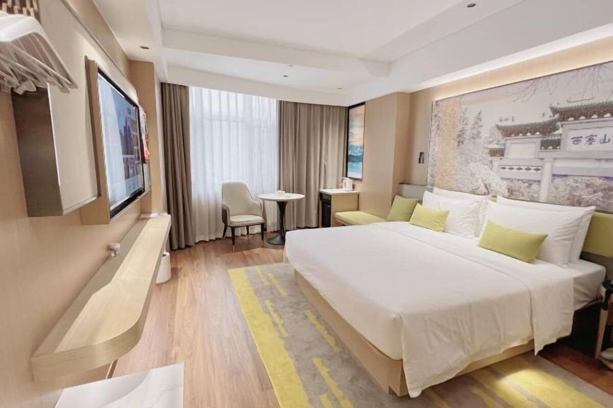 Habitación de hotel con una cama grande, un escritorio, una silla, un televisor y una ventana con cortinas.