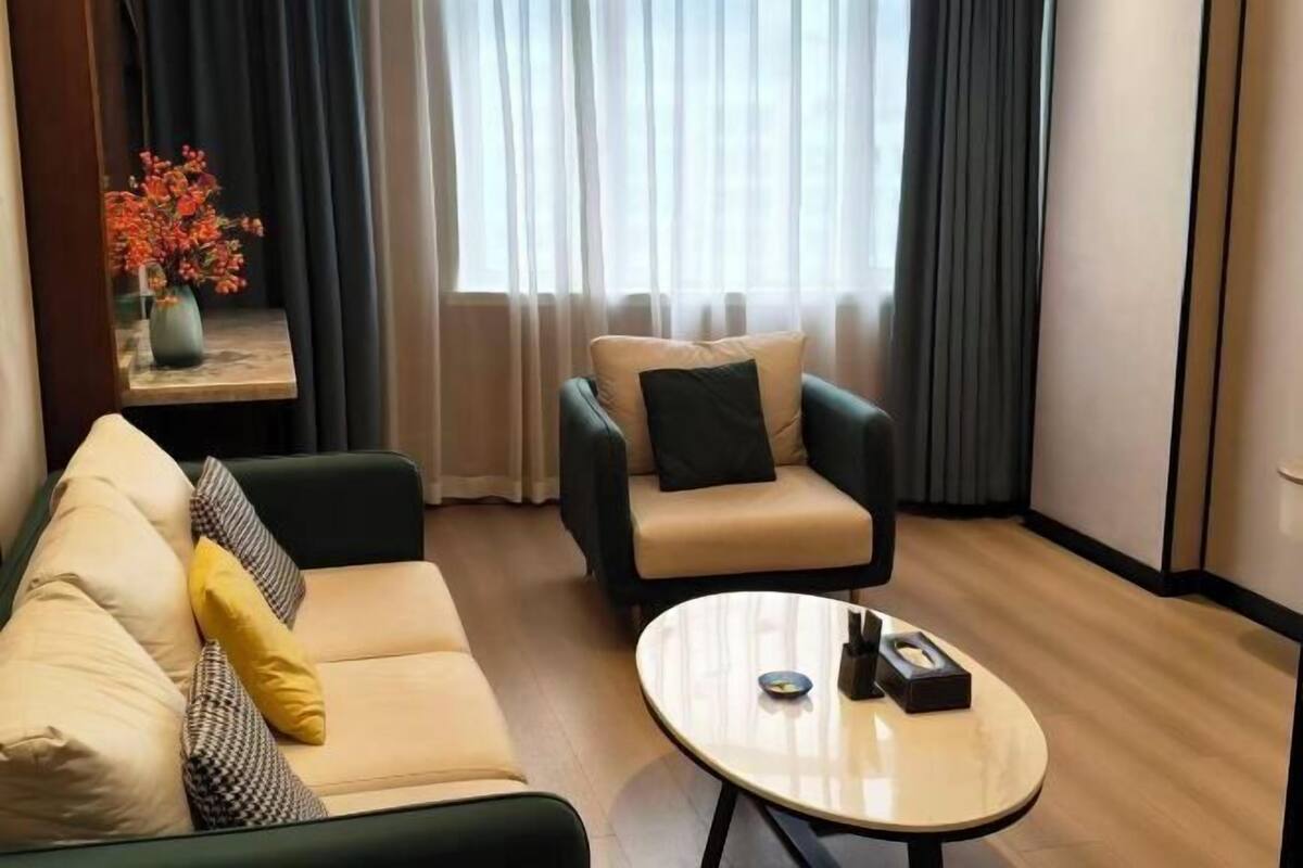 Una sala de estar moderna con un sofá color beige, un sillón negro y una mesa de centro redonda.