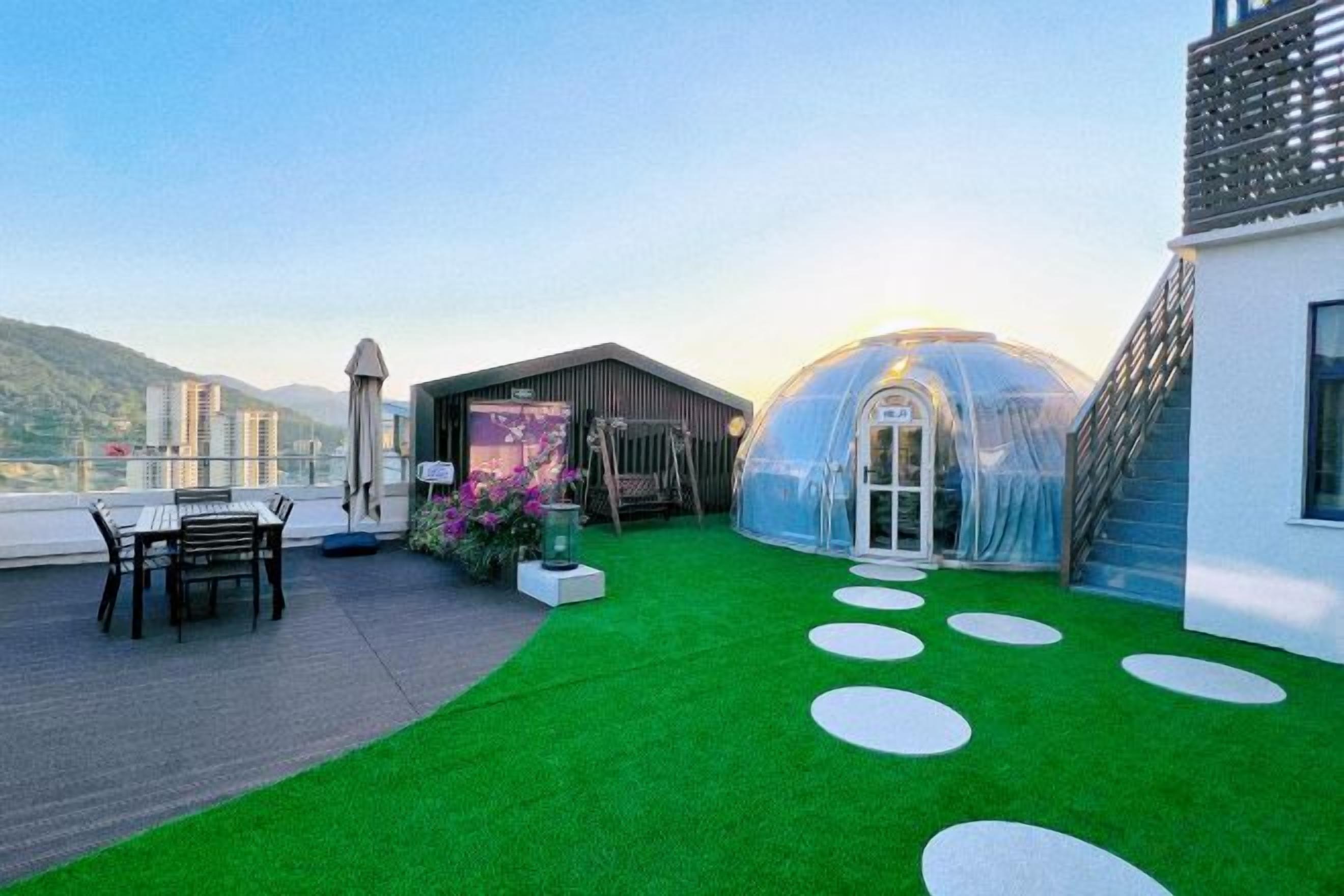 Una terraza en la azotea con césped, un invernadero de vidrio y una zona de estar.