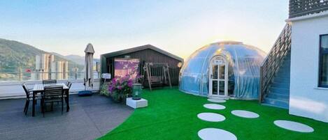 A rooftop terrace with a green lawn, a glass greenhouse, and a seating area.