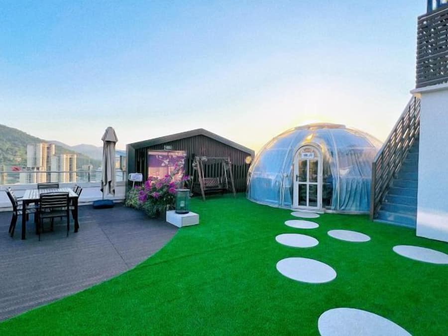A rooftop terrace with a green lawn, a glass greenhouse, and a seating area.
