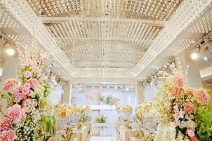 Un interior con un techo decorado con motivos florales, mesas dispuestas con arreglos florales y una ventana al fondo.