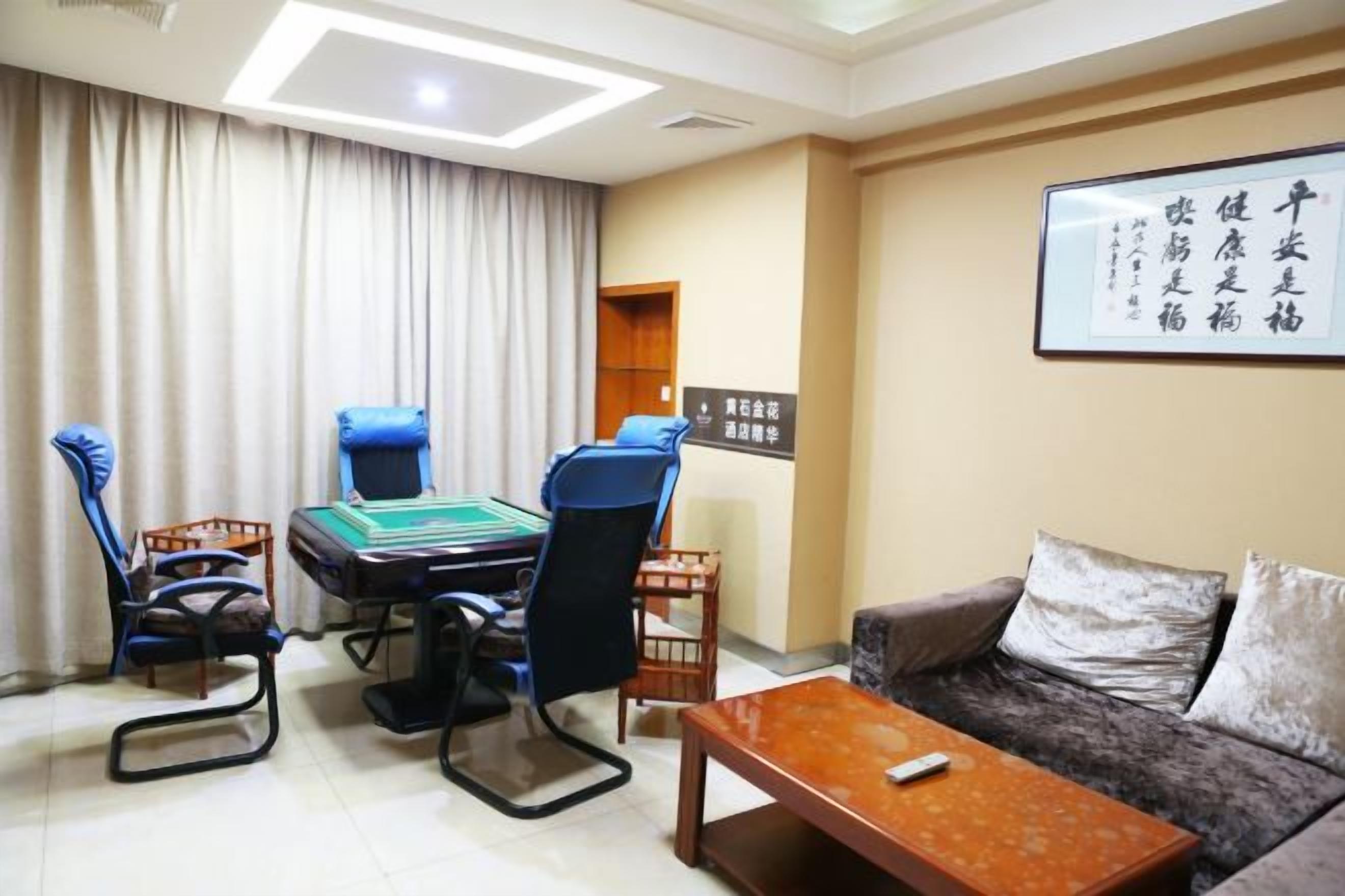 A room with a sofa, a coffee table, a gaming table with chairs, and a wall-mounted screen.