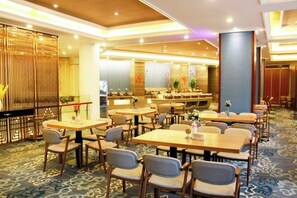 Un comedor de hotel con varias mesas y sillas, una recepción y una pared decorativa.