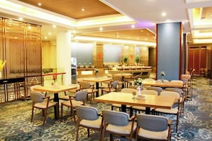 Un comedor de hotel con varias mesas y sillas, una recepción y una pared decorativa.