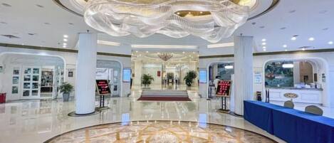 A hotel lobby with a circular marble floor, a reception desk, and a chandelier.
