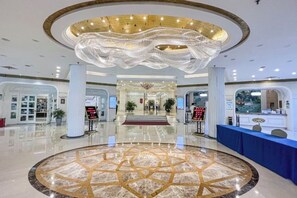Un vestíbulo de hotel con piso de mármol circular, un mostrador de recepción y una araña.