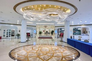 Un vestíbulo de hotel con piso de mármol circular, un mostrador de recepción y una araña.