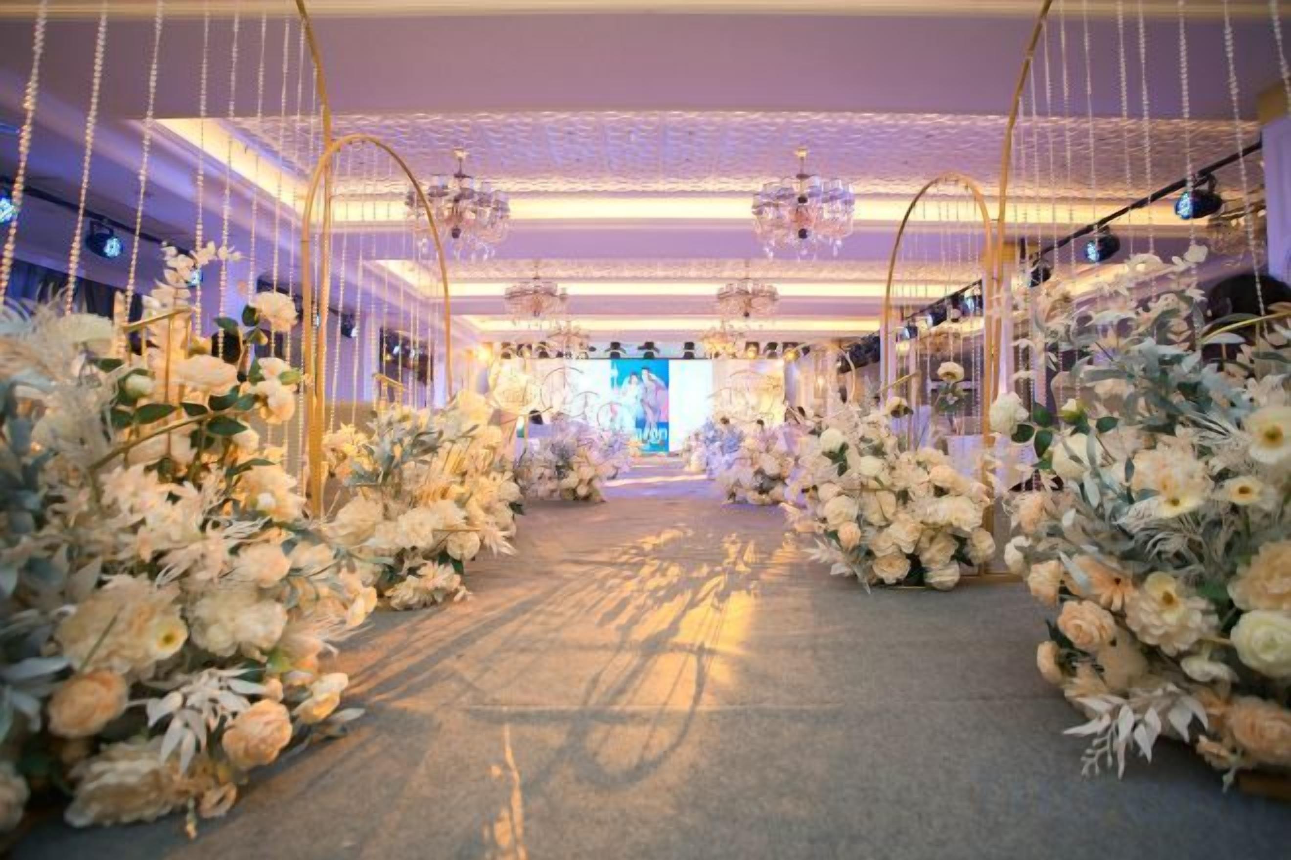 Un espacio interior con un pasillo decorado con flores, candelabros y un escenario.