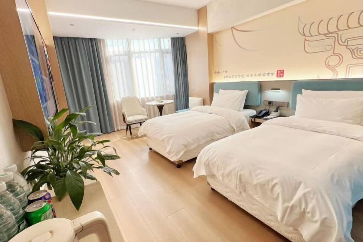 Habitación de hotel con dos camas, una mesita, una silla, una planta y una pared con diseño decorativo.